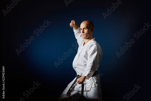 Athlete doing formal karate exercises on blue background with gradient