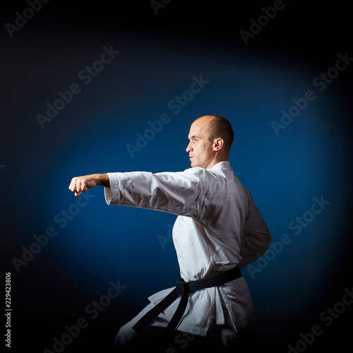 On a blue background with a gradient an adult athlete trains formal karate exercises
