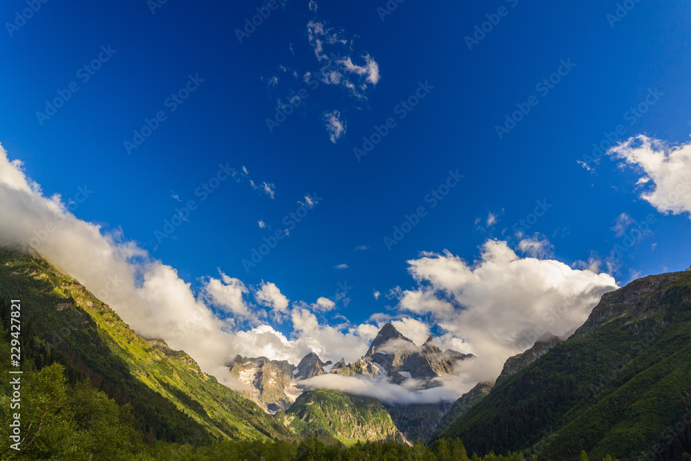 Naklejka premium Clouds over the tops of the rocky mountains overgrown with trees. Photographed in the Caucasus, Russia.
