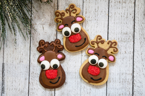 Homemade Christmas reindeer decorated sugar cookies, isolated on a wooden background with holiday garland accent © MelissaMN