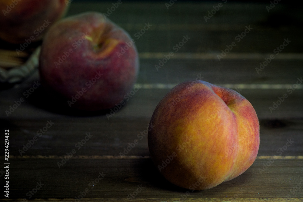 Bucket of peaches turned over with three fruits spilled from it on wooden table against black background- fall harvest composition Bucket of peaches turned over with three fruits spilled from it on wooden table against black background- fall harvest composition