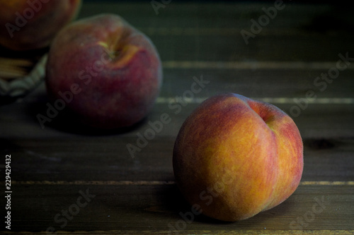 Bucket of peaches turned over with three fruits spilled from it on wooden table against black background- fall harvest composition 