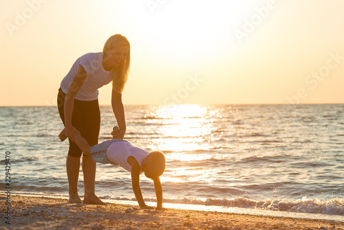 Mother and son do exercises on the beach, they meet the sunrise.Fitness, sport, yoga and healthy lifestyle concept.