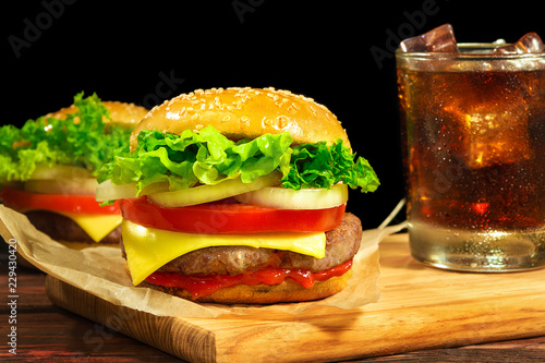 Sandwich with cutlet, cheese, tomatoes, onion, salad, ketchup and a glass of Coca Cola on a wooden board
