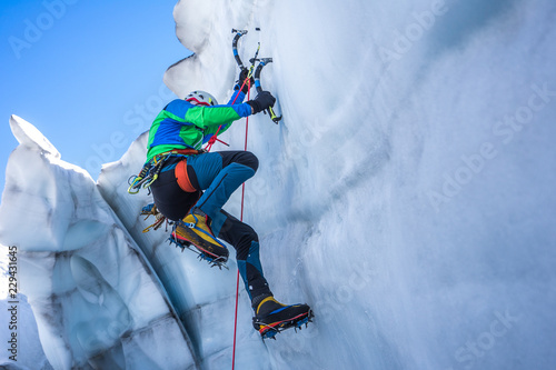 Epic shot of an ice climber climbing on a wall of ice. Mountaineer, climber or alpinist on an adventure extreme ascent with ice axe and crampons. Alpine extreme climbing on a serac or creavasse. photo