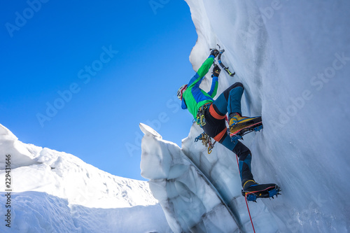 Epic shot of an ice climber climbing on a wall of ice. Mountaineer and climber on an adventure extreme ascent with ice axe and crampons. Alpine extreme climbing on a serac or creavasse.