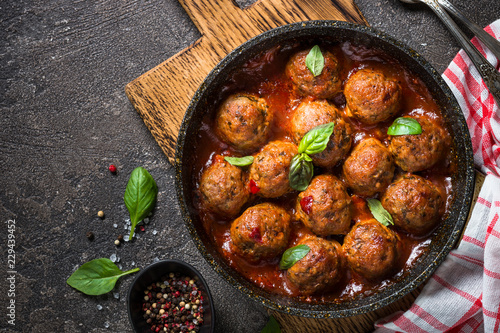 Meatballs in tomato sauce in a frying pan on dark stone table. 
