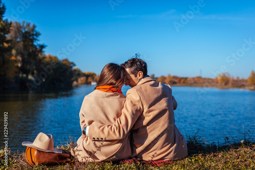 Young couple in love chilling by autumn lake. Happy man and woman enjoying nature and hugging