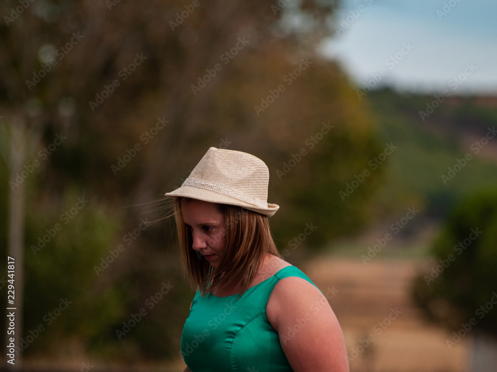 Portrait of a blond woman in a green party dress and a straw hat on the train tracks