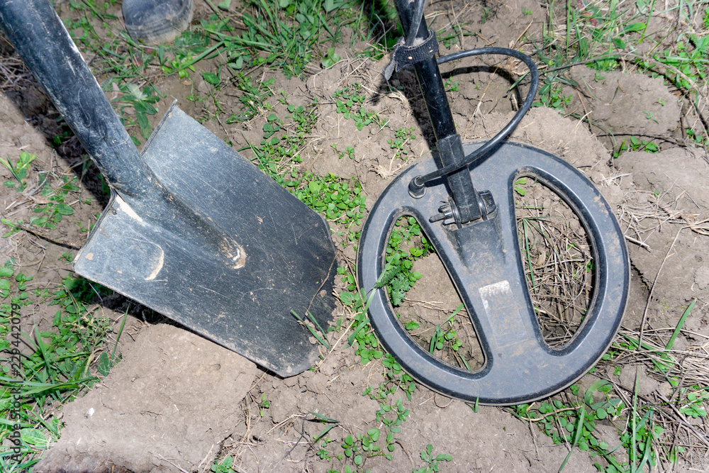 The coil of the metal detector lies on the ground, the shovel next to ...