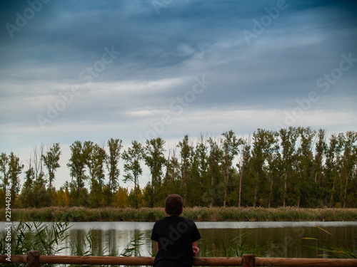 A person in a viewpoint with a wooden railing contemplating a river in autumn