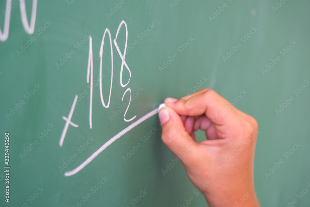 schoolgirl with chalk at the blackboard solves a math problem