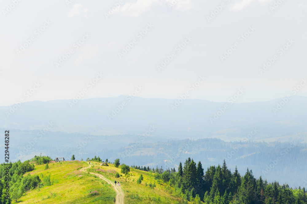 newlyweds hold hands and walk on a dirt road on top of the mountain back to the camera