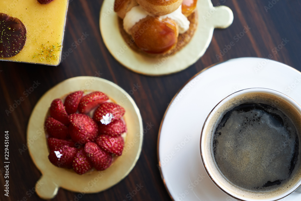 Breakfast time with cup of hot coffee and pieces of cream cake with strawberries and raspberries, sweets dessert breakfast snacks, close-up. Berry cupcakes dessert on wooden table background, top view Breakfast time with cup of hot coffee and pieces of cream cake with strawberries and raspberries, sweets dessert breakfast snacks, close-up. Berry cupcakes dessert on wooden table background, top view