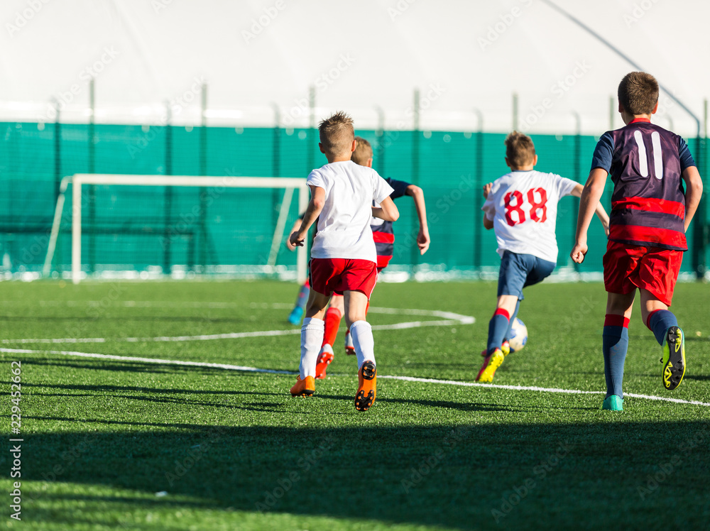 Obraz premium Junior football match. Soccer game for youth players. Boys in blue and white uniform playing soccer match. Football stadium and grassy field in the background