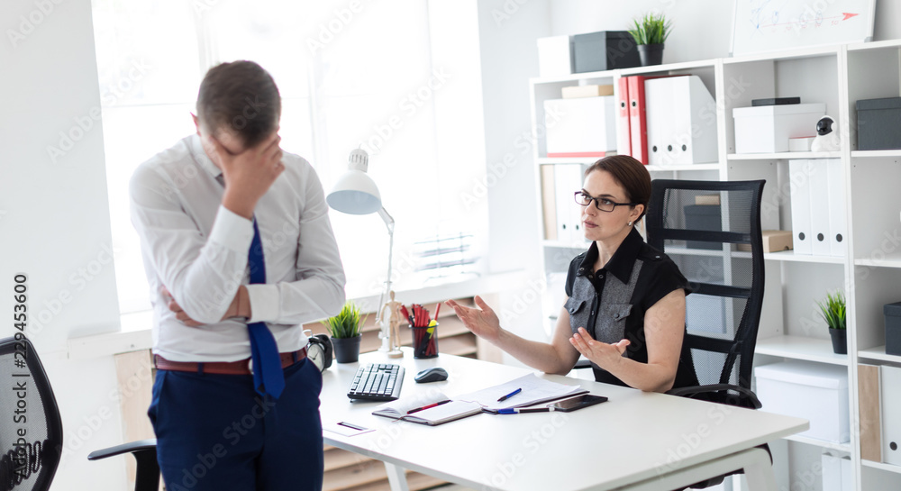 A young girl sitting in the office at the computer table. Next to her is a young man.