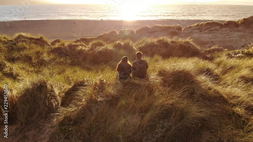 Aerial view over a young couple sitting on the beach at sunset