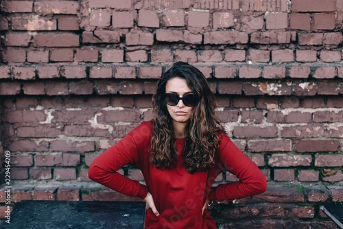  stylish young woman in red dress and sunglasses on brick wall background. fashionable long-haired girl