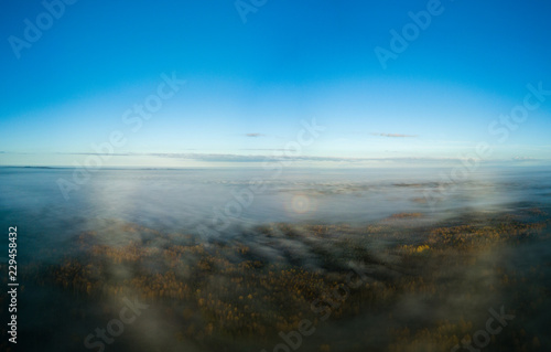 drone image. aerial view of rural area with sun halo above mist © Martins Vanags