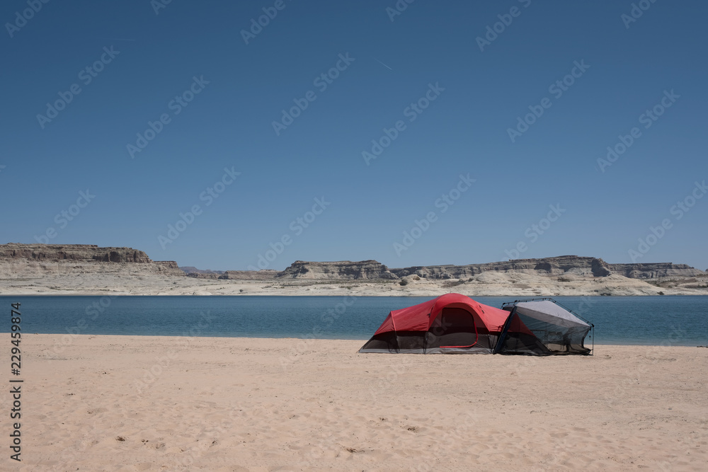 A RED TENT ON BEACH WITH BACKGROUND OF BEAUTIFUL BLUE SEA AND ROCK MOUNTAIN / BEACH CAMPING ON LAKE POWELL , UTAH , ARIZONA , USA