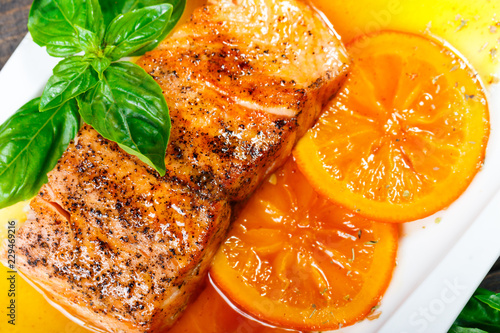 Honey Glazed fillet salmon with orange slices, spices and basil on white plate on dark background. Delicious dish of seafood.