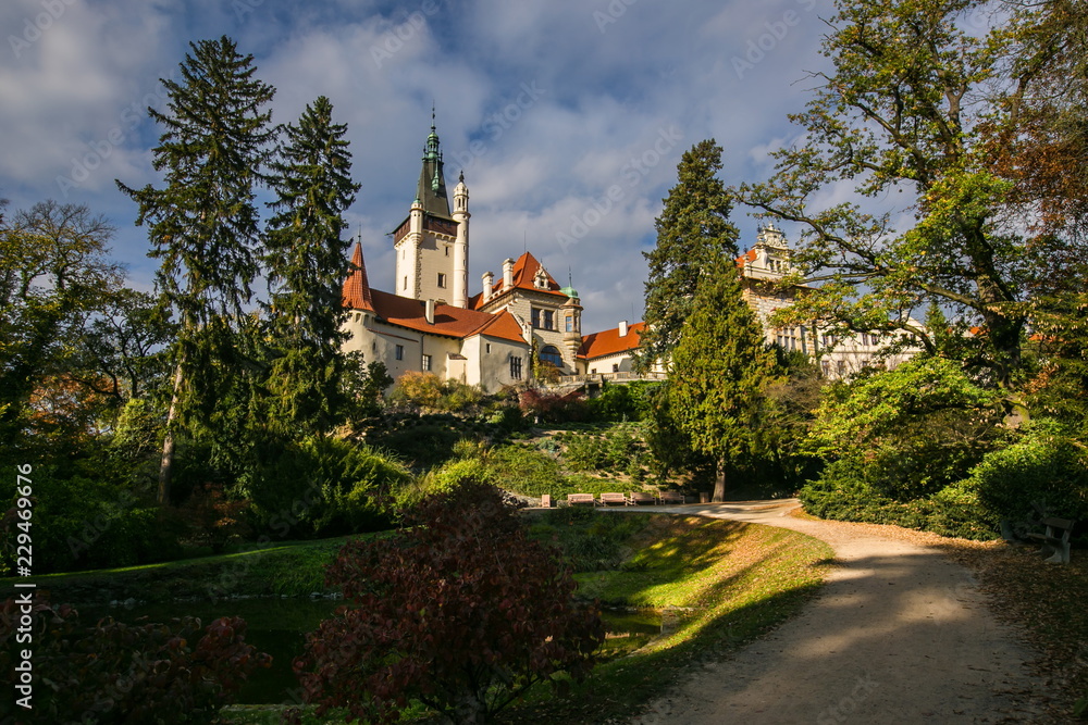 Fototapeta premium Scenic landscape of famous romantic Pruhonice castle, Czech Republic, Europe, standing on hill in a park, sunny fall day, blue sky, colorful trees, foot path with shadows of trees