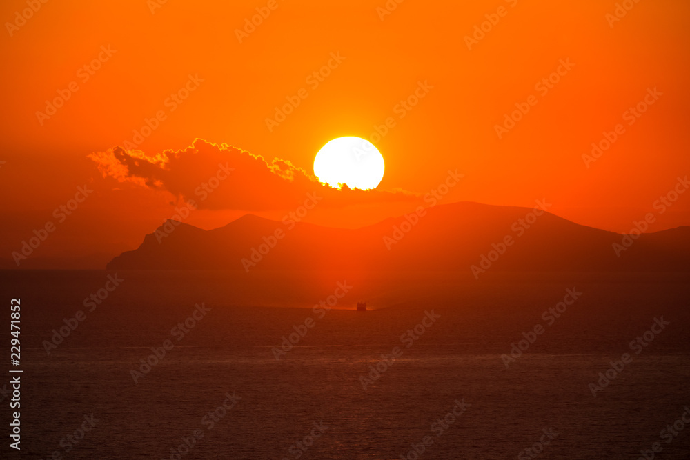 Dramatic red sundown with a sailboat or yacht sailing to coastline Dramatic red sundown with a sailboat or yacht sailing to coastline