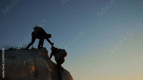 silhouette two men teamwork tourists climber climbs a mountain. walking tourist hiking adventure climbers sunset climb the mountain . slow motion video. hiker sunlight on top win victory the hill
