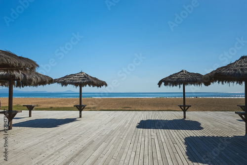 Empty beach  straw umbrellas on wooden flooring  bright sunny day  no season