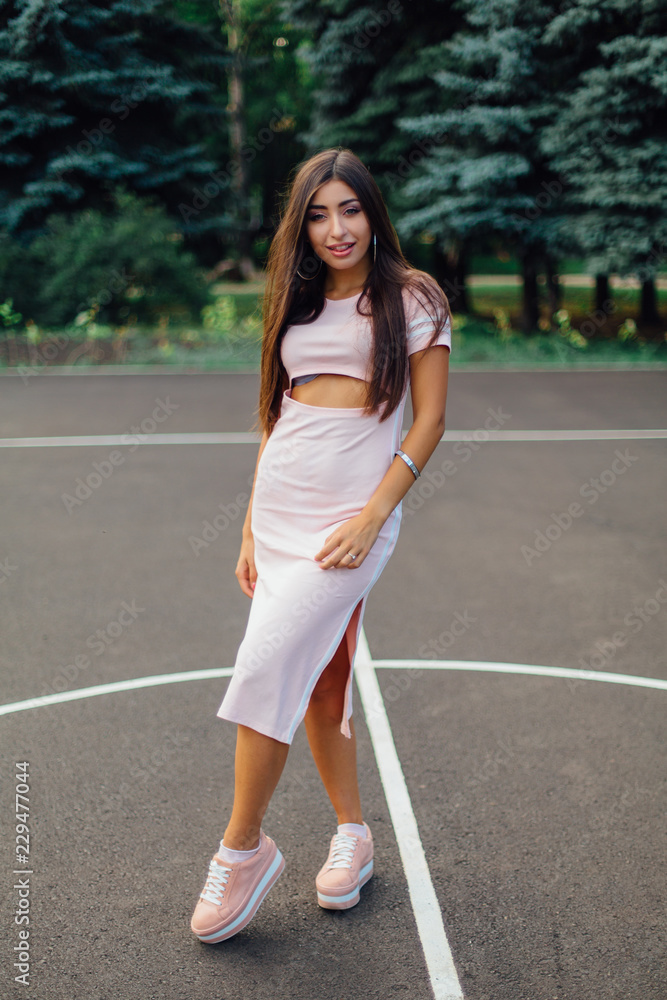 Charming brunette female dressed in a pink dress posing on the basketball court. Charming brunette female dressed in a pink dress posing on the basketball court.