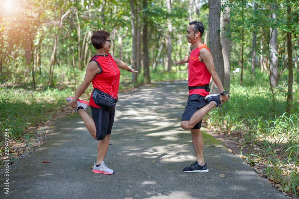 Fototapeta premium Happy senior asian woman with man or personal trainer stretch thigh muscles at park. Athletic senior exercising together outdoor. Elderly care exercise sport activity concept