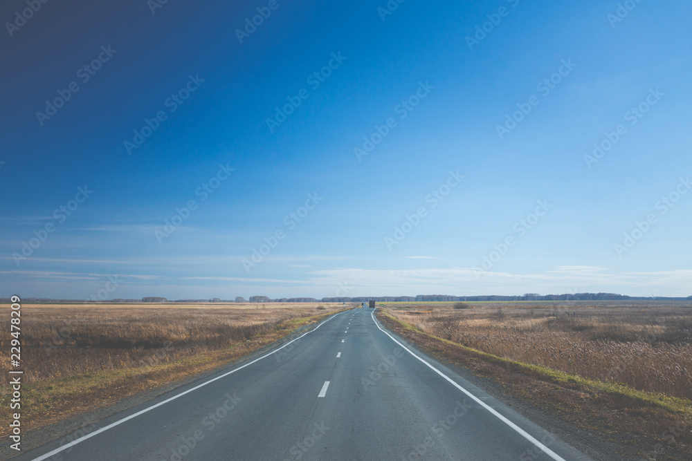 Empty road through the autumn fields. Toned image.