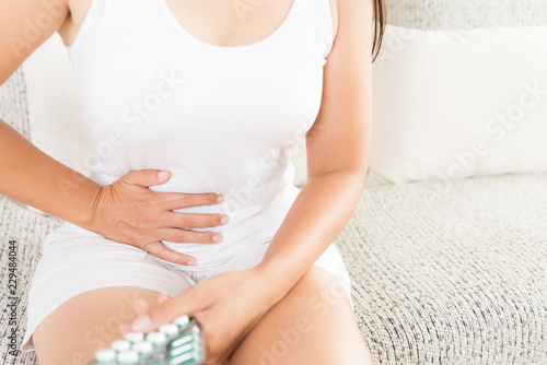 Young woman having painful stomachache sitting on sofa at home. Chronic gastritis. Abdomen bloating concept.