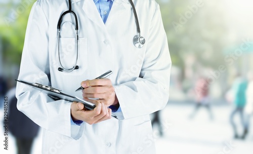 Doctor with stethoscope writing on background