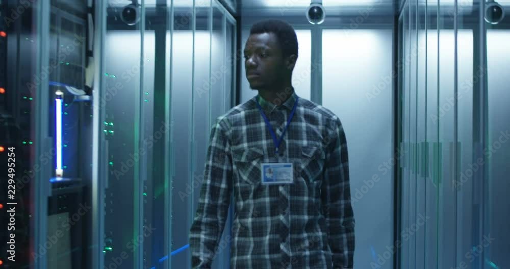 African American system administrator walks over to the server rack and ...