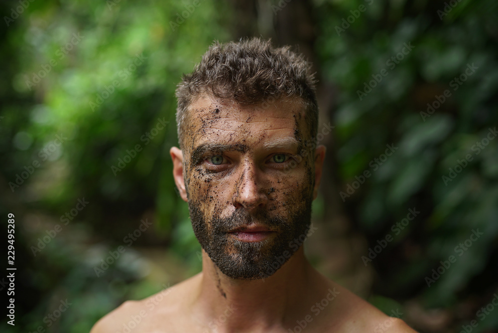 Foto de Close-up of a young handsome man with dirty face looks intently at  the camera in a wild forest do Stock | Adobe Stock