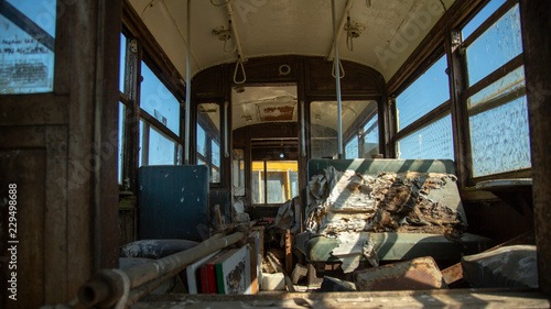 Sunlit inside low perspective of old passenger train car with torn and worn seats and debris with blue sky showing through windows