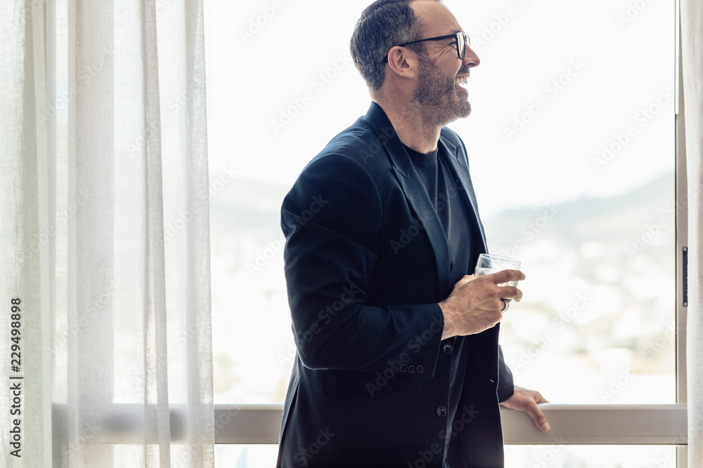 Mid adult businessman with glass of drink in hotel room Mid adult businessman with glass of drink in hotel room