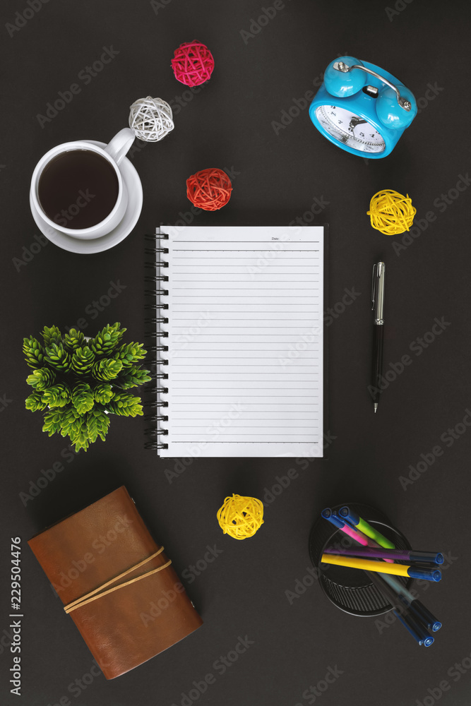 Notepad, coffee and alarm clock on black background. Office table still life.
