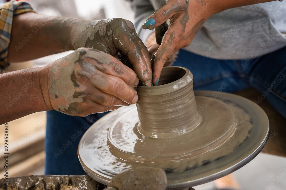 Potter makes on the pottery wheel clay pot. The hands of a potter with the tool, close-up Potter makes on the pottery wheel clay pot. The hands of a potter with the tool, close-up
