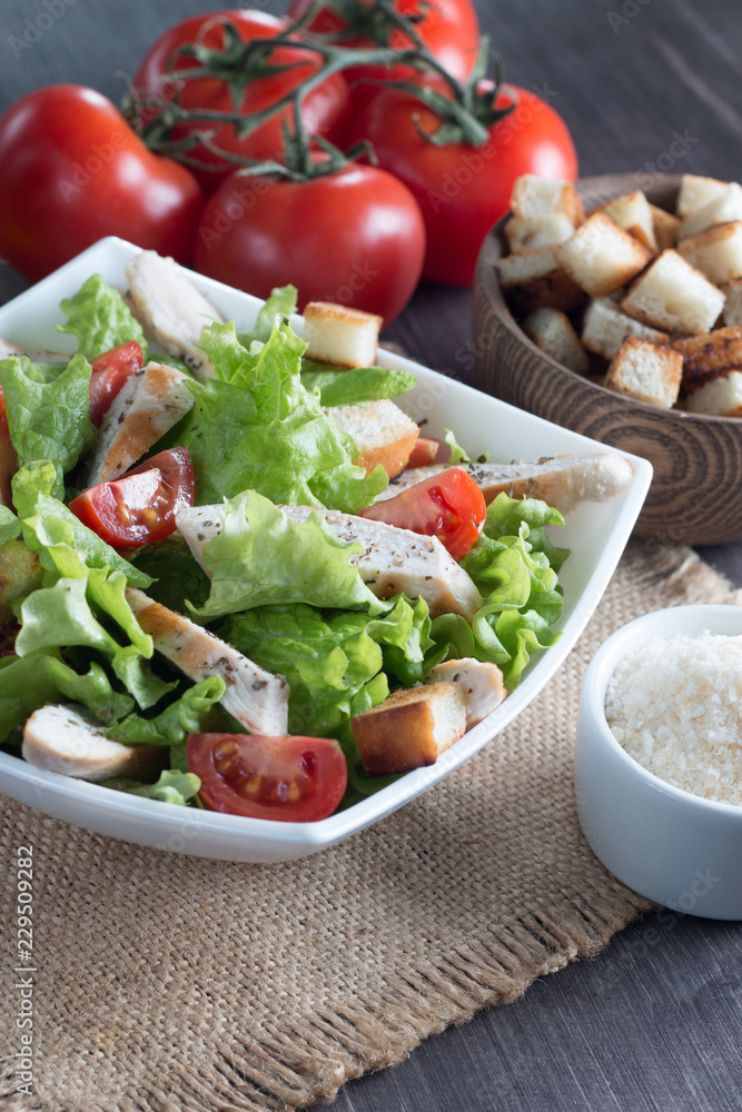 Fresh salad with delicious chicken breast, ruccola, spinach, cabbage, arugula and tomato on wooden background. Oil, salt and pepper.