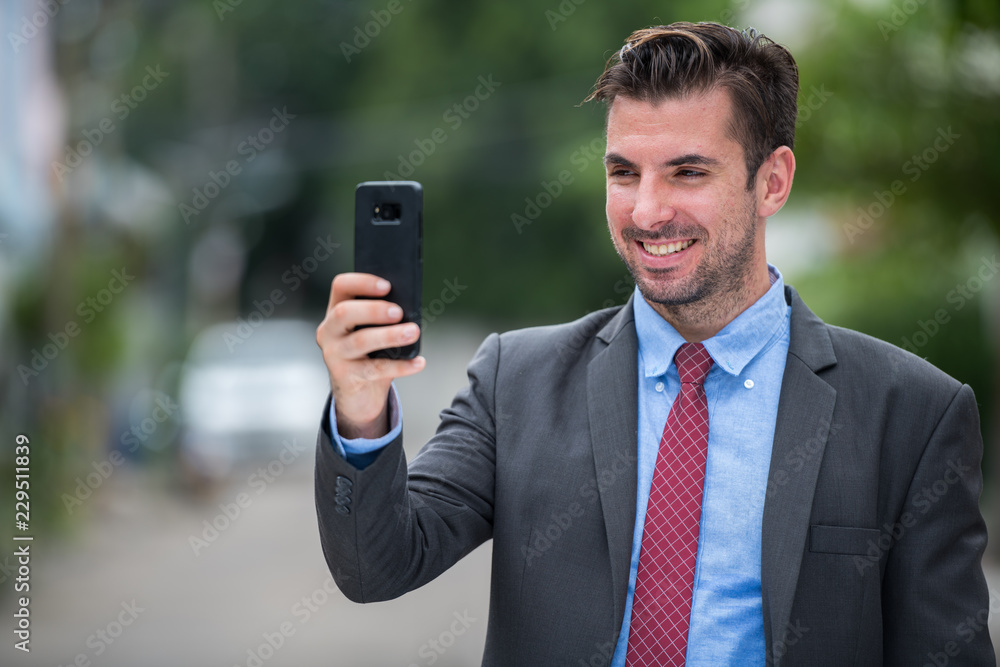 Young happy Hispanic businessman smiling while using phone outdoors Young happy Hispanic businessman smiling while using phone outdoors