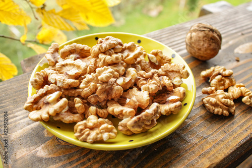 Walnuts in a yellow plate on the background of antique wood and yellow leaves. Warm sunny day golden autumn