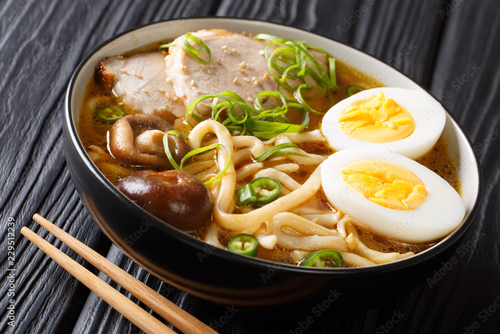 Asian style soup with udon noodles, pork, boiled eggs, mushrooms and green onions close-up on the table. horizontal