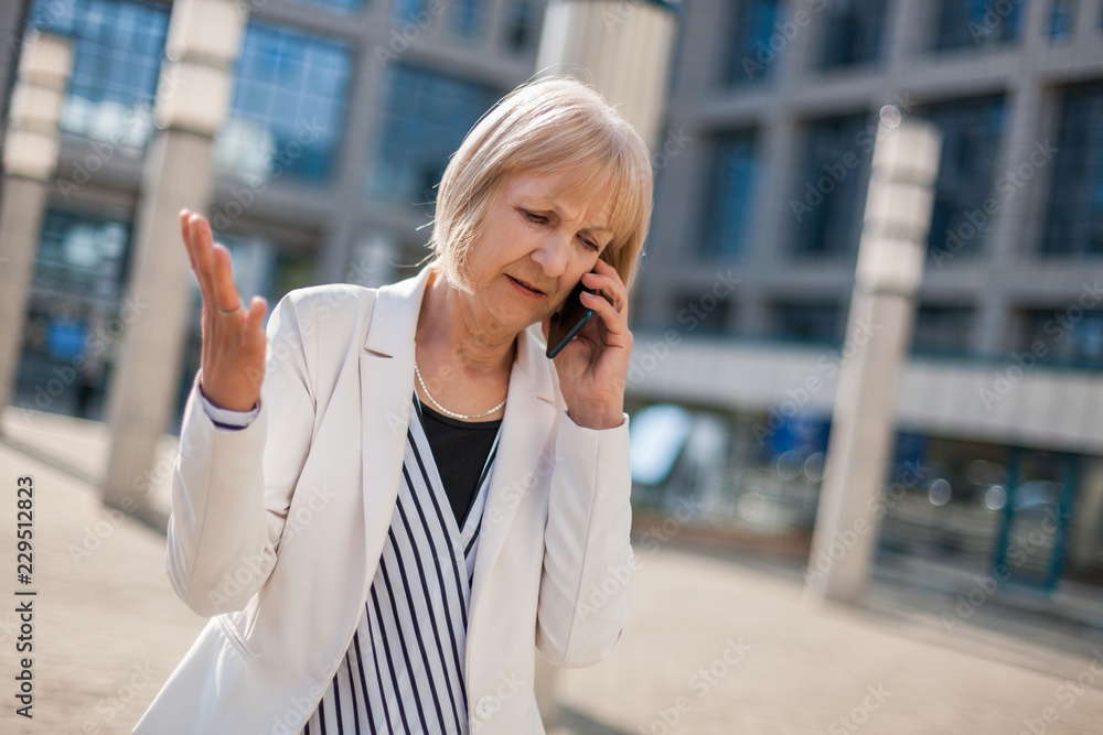 Outdoor portrait of angry senior businesswoman who is talking on phone. Outdoor portrait of angry senior businesswoman who is talking on phone.