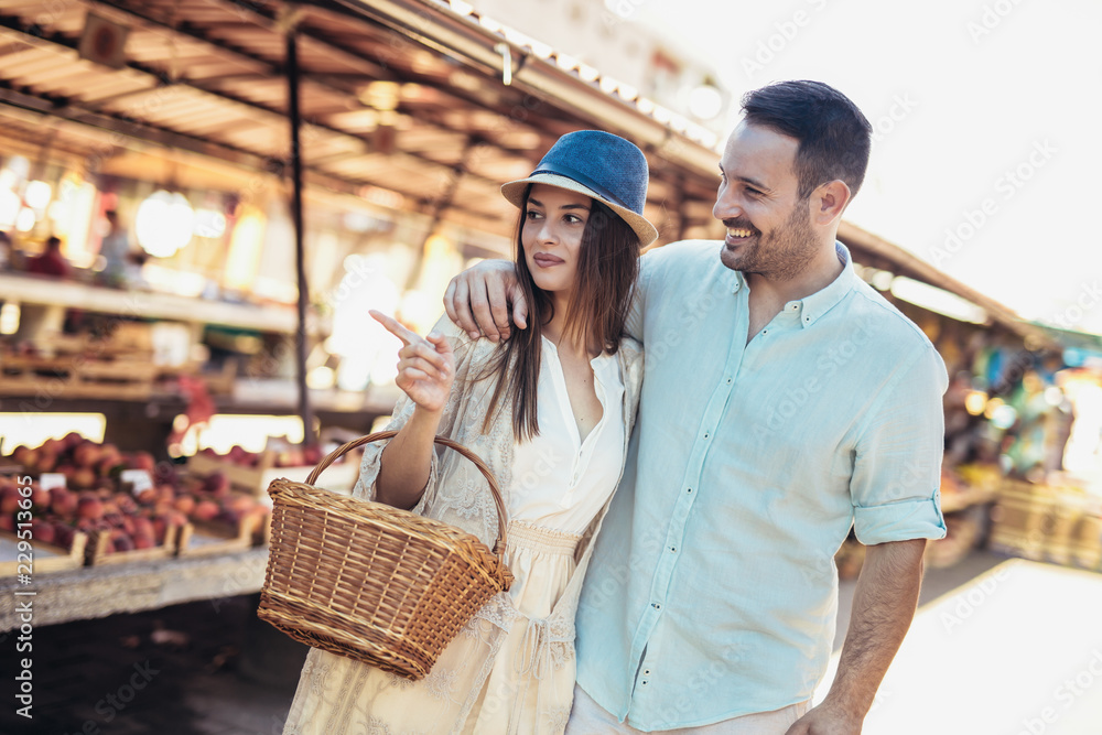 Young couple buying fruits and vegetables in a market on a sunny morning. Young couple buying fruits and vegetables in a market on a sunny morning.