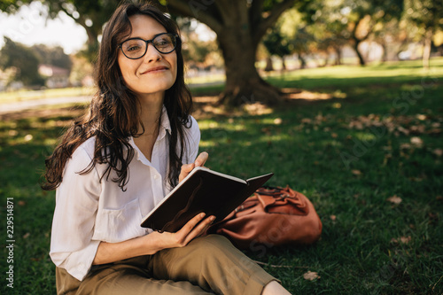 Pretty woman writing in book at park