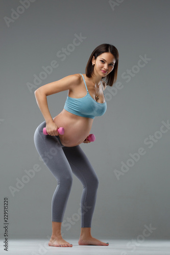Fototapeta Naklejka Na Ścianę i Meble -  Slim pregnant woman is engaged in fitness isolated on gray background.