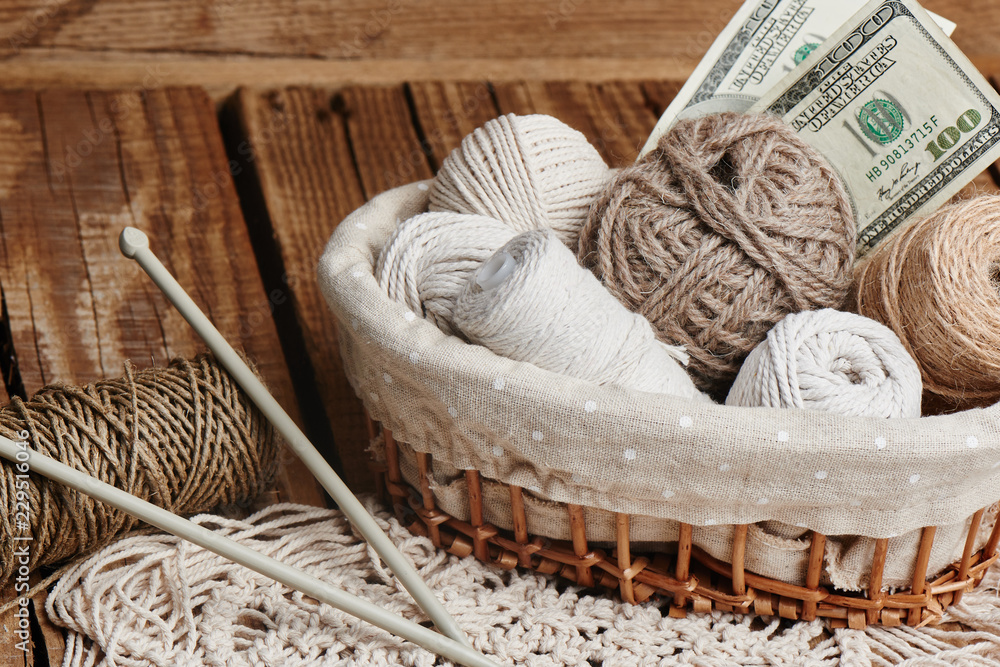 Profitable hobby. Earnings on needlework. Balls of natural color yarn, knitting needles and money on a wooden table. Profitable hobby. Earnings on needlework. Balls of natural color yarn, knitting needles and money on a wooden table.