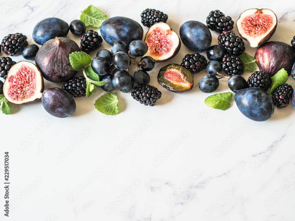 Purple fruits, berries and mint leaves border. Blackberries, grapes, plums and figs on white marble background. Tasty and ripe fruits and berries. Copy space Top view Purple fruits, berries and mint leaves border. Blackberries, grapes, plums and figs on white marble background. Tasty and ripe fruits and berries. Copy space Top view